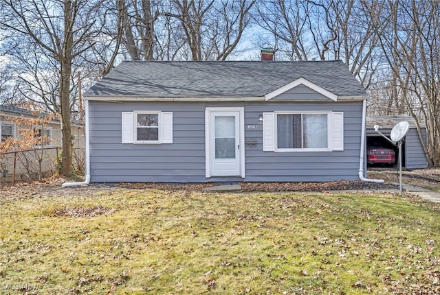 bungalow with a shingled roof, fence, a front lawn, and a carport