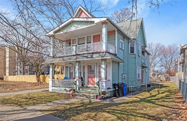 view of front of home featuring a porch, a balcony, fence, roof with shingles, and a front yard