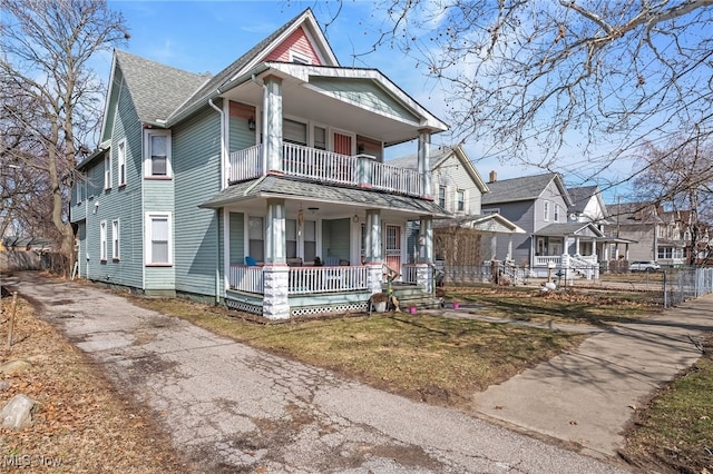 victorian home with a porch, a shingled roof, a front yard, fence, and a balcony