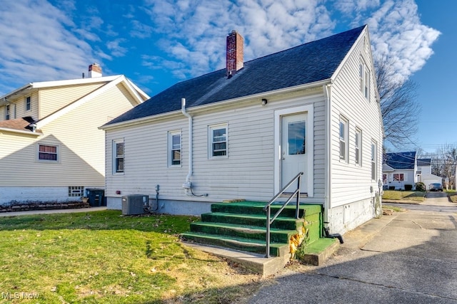 rear view of property featuring entry steps, a chimney, roof with shingles, a yard, and central AC