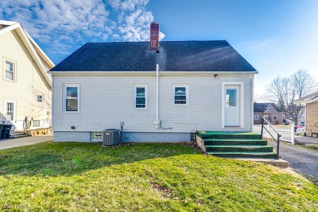 rear view of house featuring roof with shingles, a chimney, central AC unit, and a yard