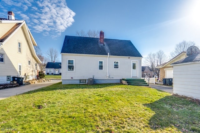 back of property with a chimney, central AC unit, a lawn, and roof with shingles