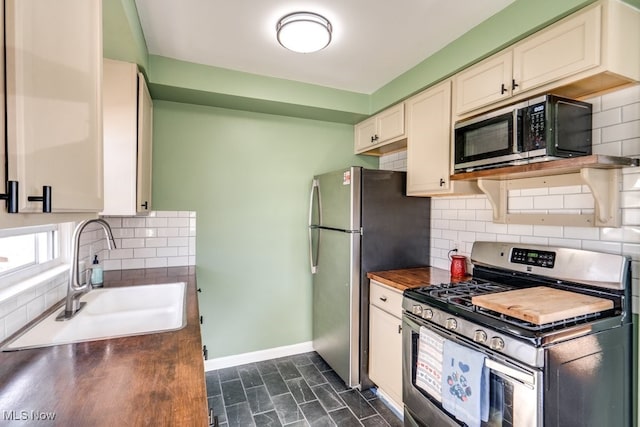 kitchen with appliances with stainless steel finishes, a sink, backsplash, and baseboards