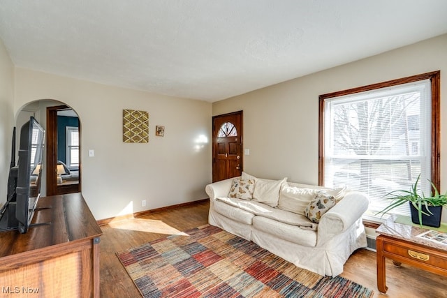 living room featuring arched walkways, baseboards, and wood finished floors