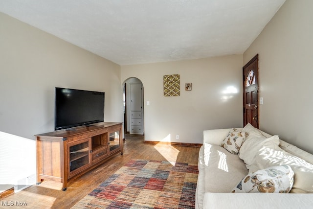 living room featuring baseboards, arched walkways, and wood finished floors