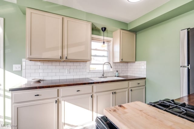 kitchen featuring a sink, white cabinets, hanging light fixtures, freestanding refrigerator, and decorative backsplash