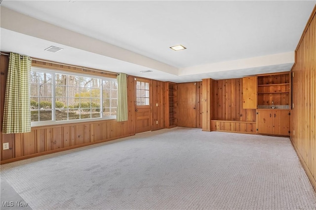 unfurnished room featuring carpet floors, wood walls, visible vents, and baseboards