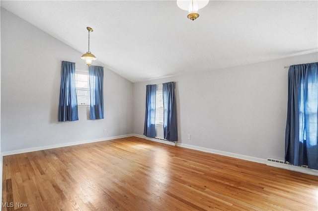 spare room featuring lofted ceiling, baseboard heating, light wood-type flooring, and baseboards