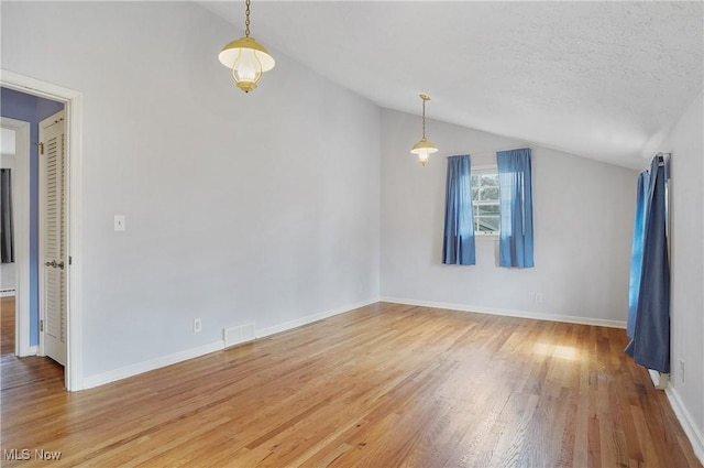 spare room with lofted ceiling, visible vents, baseboards, and wood finished floors