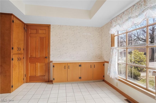 empty room featuring light tile patterned floors, visible vents, baseboards, a tray ceiling, and wallpapered walls