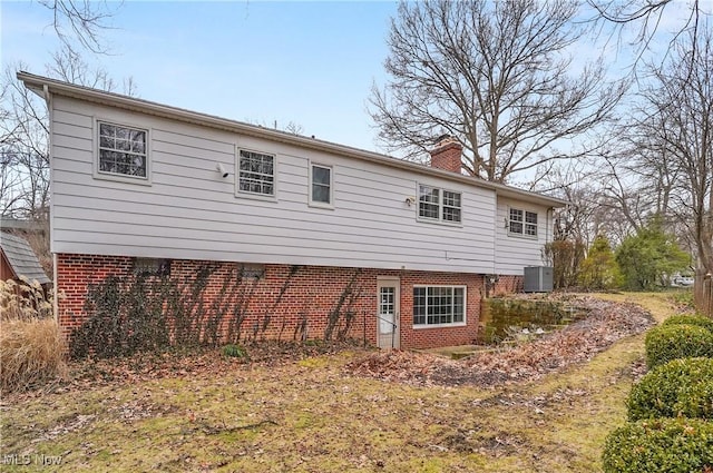 rear view of property featuring brick siding, a chimney, and cooling unit