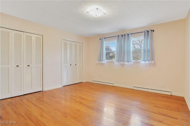 unfurnished bedroom with a baseboard heating unit, two closets, hardwood / wood-style flooring, and baseboards