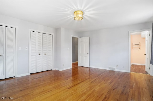 unfurnished bedroom featuring light wood finished floors, baseboards, visible vents, ensuite bath, and two closets