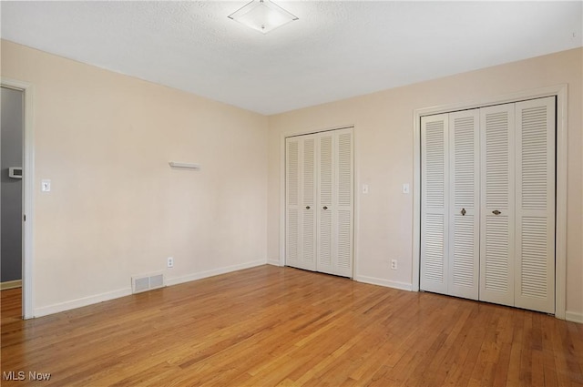 unfurnished bedroom featuring baseboards, visible vents, light wood finished floors, and two closets