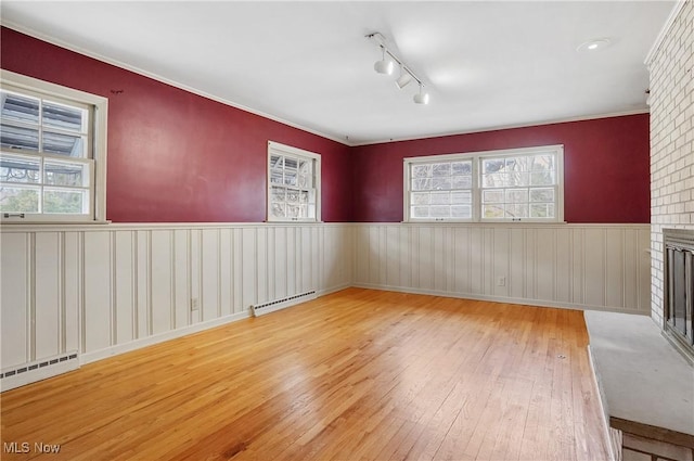 empty room with a baseboard radiator, a brick fireplace, wainscoting, and hardwood / wood-style floors