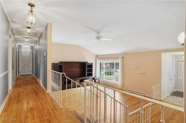 hall featuring lofted ceiling, a baseboard heating unit, wood finished floors, visible vents, and an upstairs landing