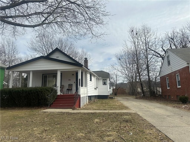 bungalow featuring covered porch, a chimney, and concrete driveway