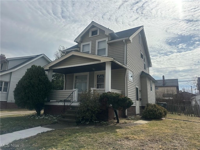 view of front of home featuring covered porch, fence, and a front lawn