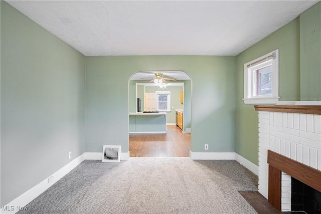 unfurnished living room with a healthy amount of sunlight, a fireplace, visible vents, and arched walkways