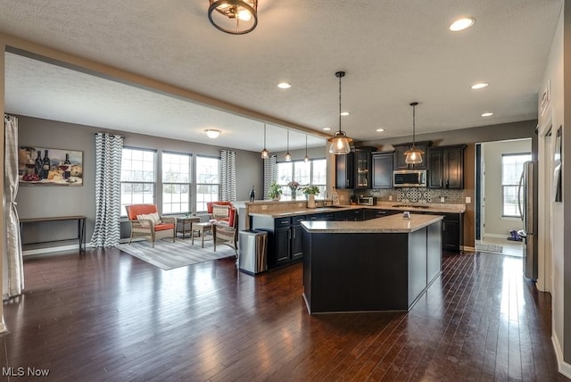 kitchen with stainless steel appliances, a peninsula, dark wood-style flooring, light countertops, and tasteful backsplash