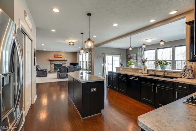 kitchen featuring a stone fireplace, dark cabinets, a sink, black dishwasher, and stainless steel fridge