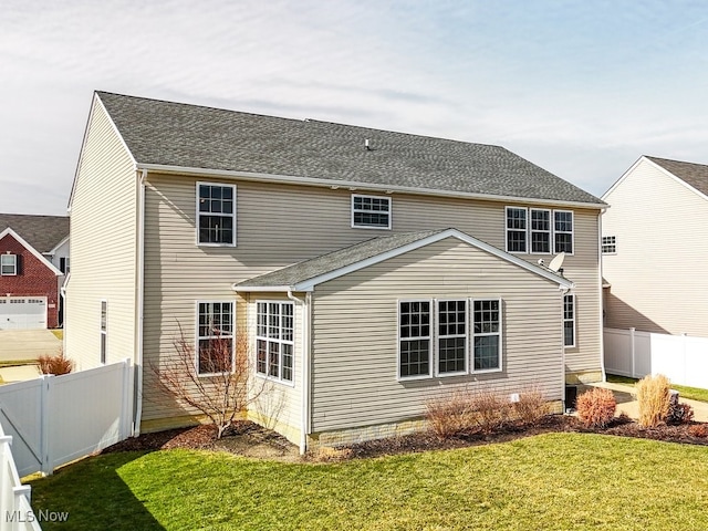 back of house with a shingled roof, a lawn, and fence