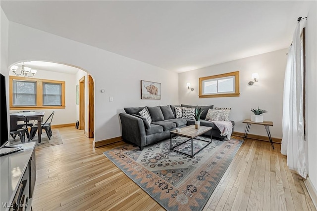 living room featuring arched walkways, light wood finished floors, a chandelier, and baseboards