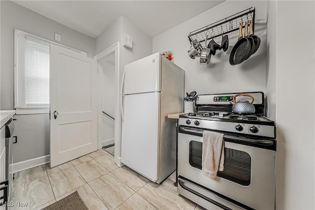 kitchen with baseboards, gas stove, freestanding refrigerator, light countertops, and light tile patterned flooring