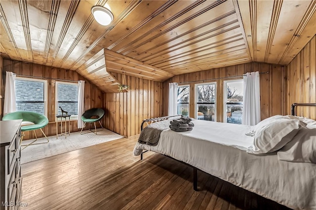 bedroom featuring vaulted ceiling, multiple windows, wood-type flooring, and wooden walls