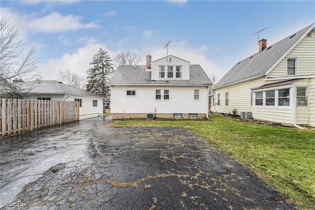 back of property with central AC unit, a lawn, a shingled roof, and fence