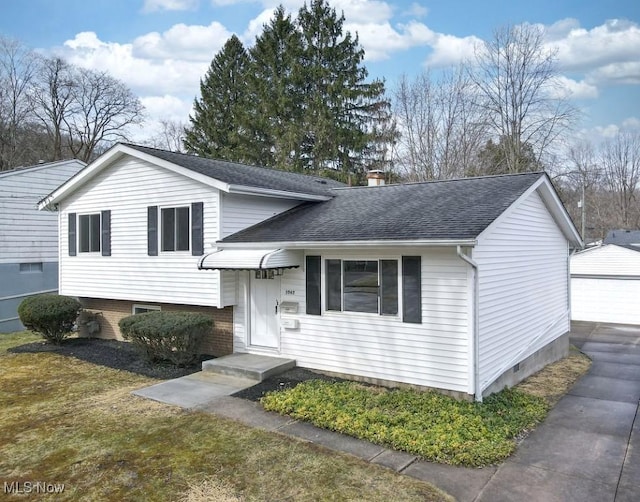 tri-level home featuring an outbuilding, a garage, roof with shingles, a front lawn, and a chimney