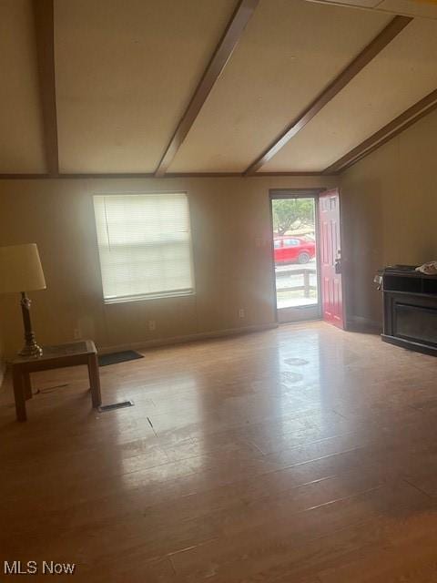 unfurnished living room featuring beam ceiling, baseboards, and wood finished floors