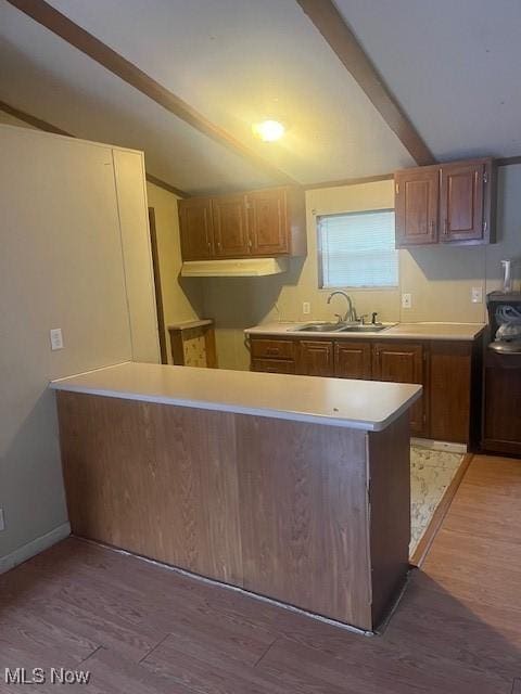 kitchen with vaulted ceiling with beams, light wood-style flooring, light countertops, and a sink