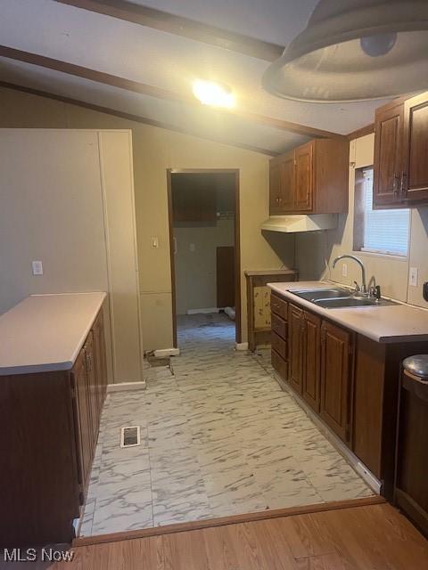 kitchen featuring lofted ceiling, light countertops, light wood finished floors, and a sink