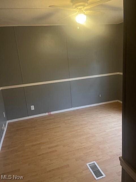 empty room with visible vents, ceiling fan, baseboards, and wood finished floors