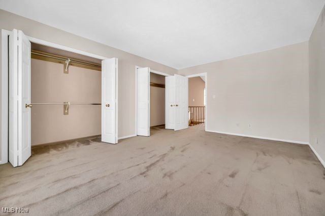 unfurnished bedroom featuring carpet floors, baseboards, and multiple closets