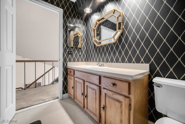 half bath featuring tile patterned floors, vanity, toilet, and wallpapered walls