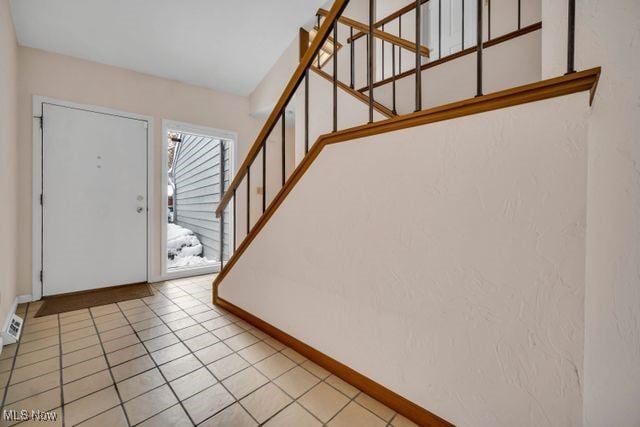 entryway featuring stairway, light tile patterned flooring, and baseboards