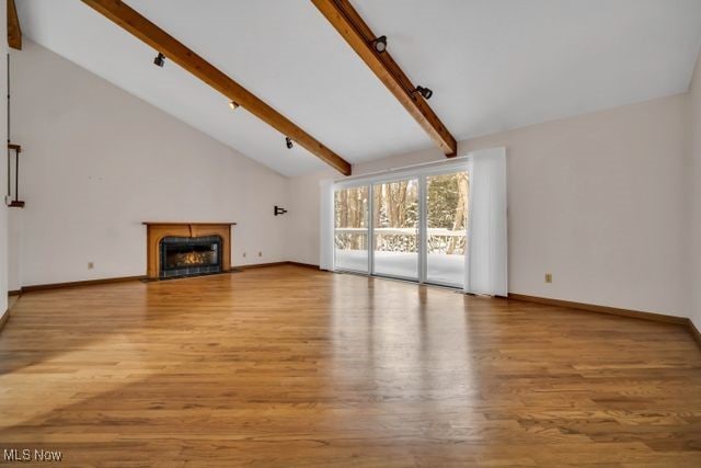 unfurnished living room featuring a fireplace with flush hearth, high vaulted ceiling, beam ceiling, and wood finished floors