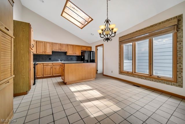 kitchen featuring a skylight, decorative light fixtures, light tile patterned floors, freestanding refrigerator, and a chandelier