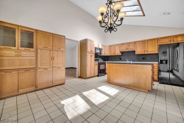 kitchen featuring decorative backsplash, a center island, black appliances, a notable chandelier, and light tile patterned flooring