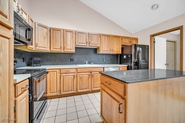 kitchen featuring tasteful backsplash, lofted ceiling, black appliances, a sink, and light tile patterned flooring