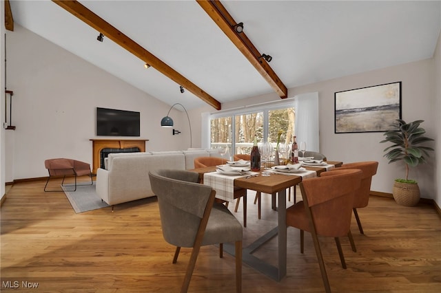 dining room with vaulted ceiling with beams, light wood-type flooring, a fireplace, and baseboards