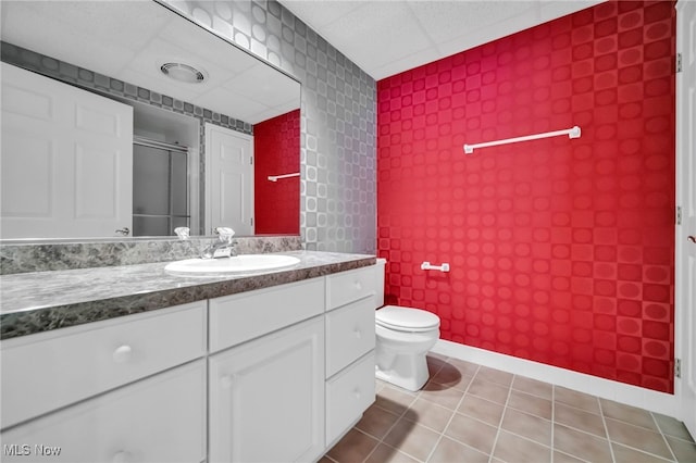 bathroom with a drop ceiling, toilet, a shower with door, tile patterned flooring, and vanity