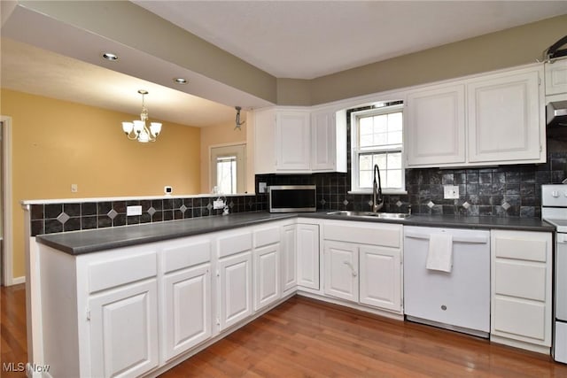 kitchen featuring white appliances, dark countertops, a peninsula, a sink, and a wealth of natural light