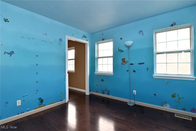 empty room with baseboards, visible vents, and wood finished floors