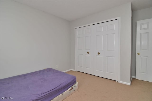 bedroom with a closet, light carpet, and baseboards