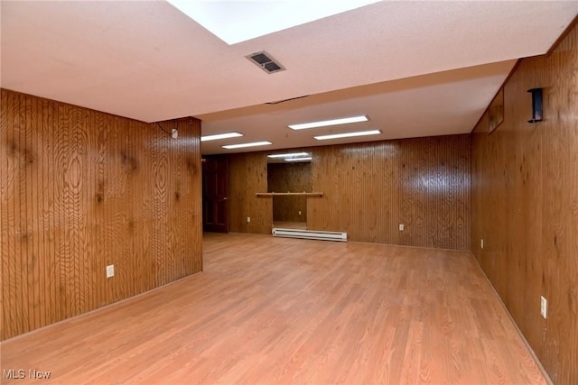 finished below grade area featuring wooden walls, visible vents, baseboard heating, and wood finished floors