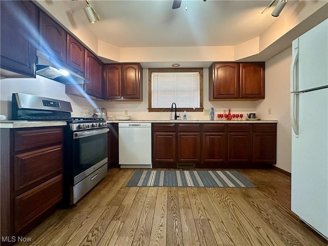 kitchen with white appliances, under cabinet range hood, dark wood-style floors, and a sink