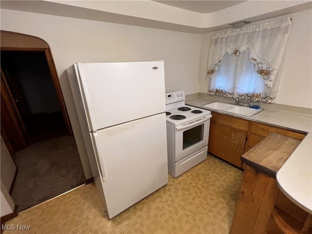 kitchen featuring light floors, light countertops, brown cabinetry, a sink, and white appliances